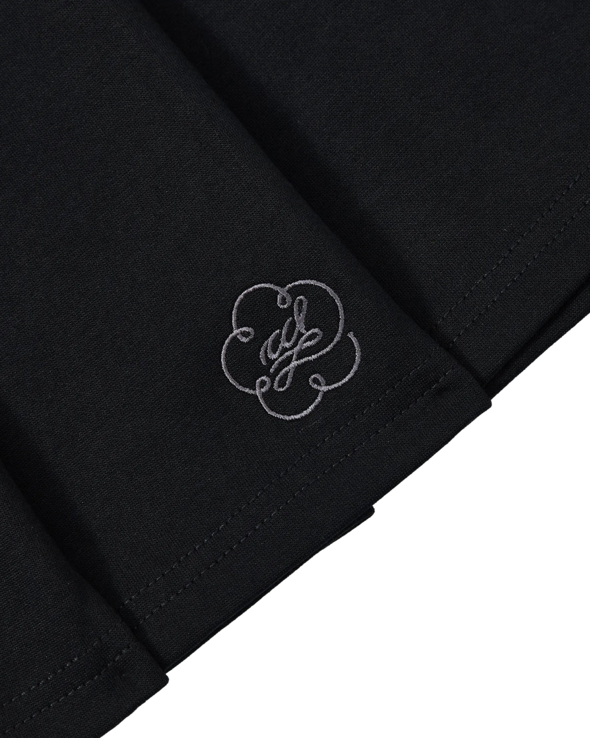 Close-up of the BLACK KONA MIDI SKIRT by Sundae School, showing its black fabric with a white embroidered swirl and loop detail near the hem.