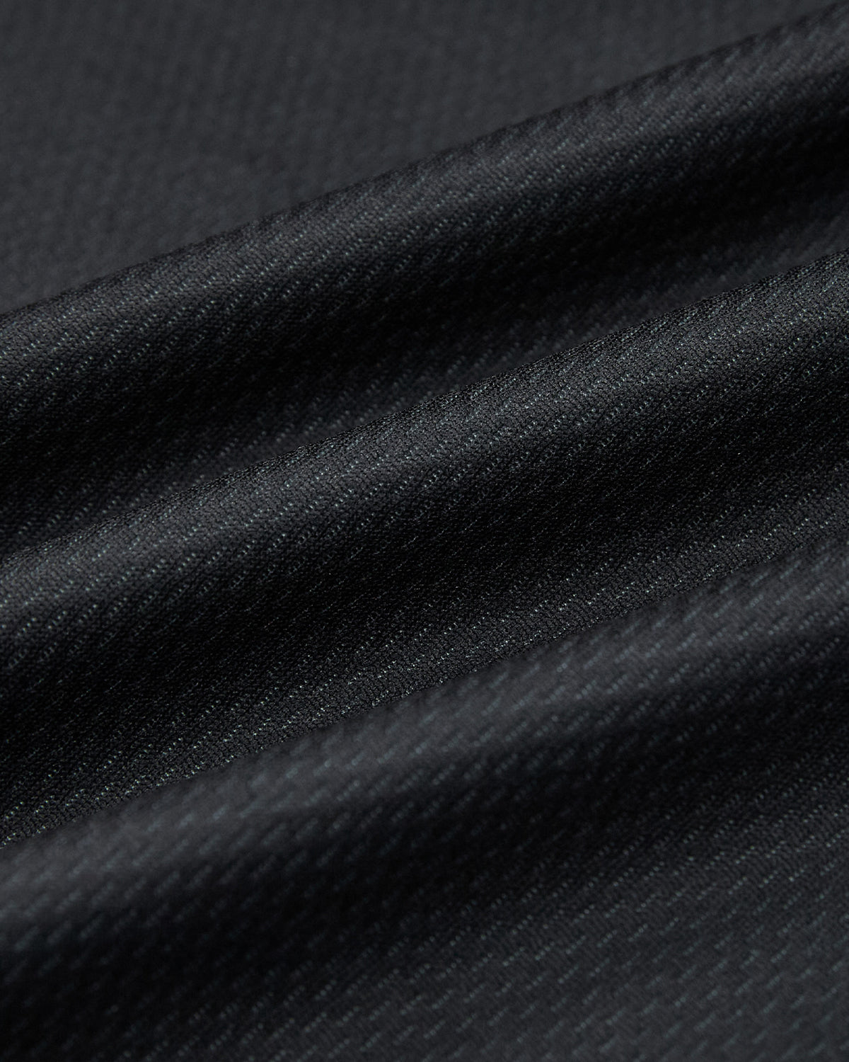 Close-up of black textured fabric with diagonal ridges and soft folds, highlighting the smooth, subtly shiny surface—perfect for the KOREATOWN FOOTBALL JERSEY by Sundae School, featuring a fine weave and subtle pattern.