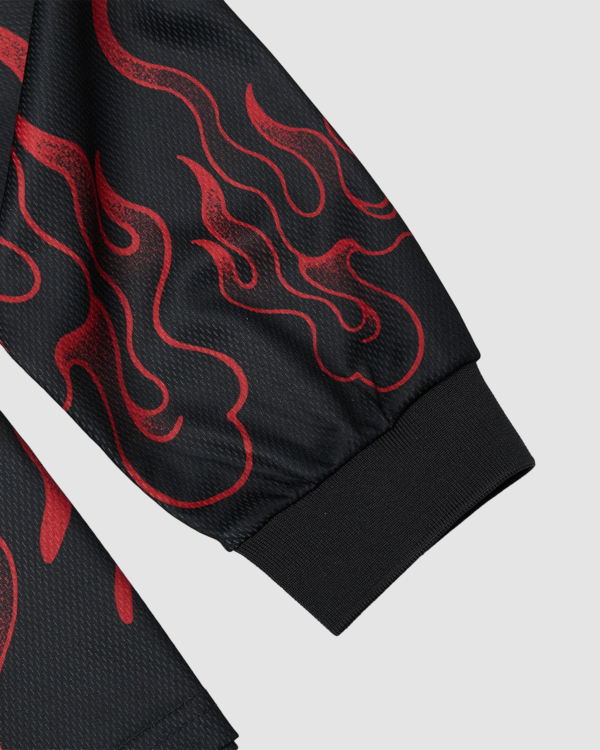 A close-up of the Sundae School KOREATOWN FOOTBALL JERSEY’s black sleeve, adorned with red flame graphics and a ribbed cuff inspired by Korean designs, set on a light gray background.