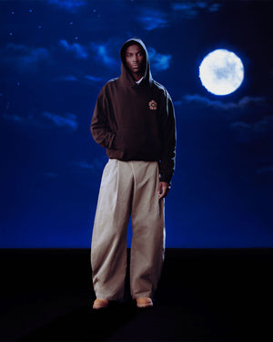 Someone wearing the Sundae School HIGH HORSE LNY HOODIE and wide, light trousers stands beneath a night sky with a full moon and scattered clouds.