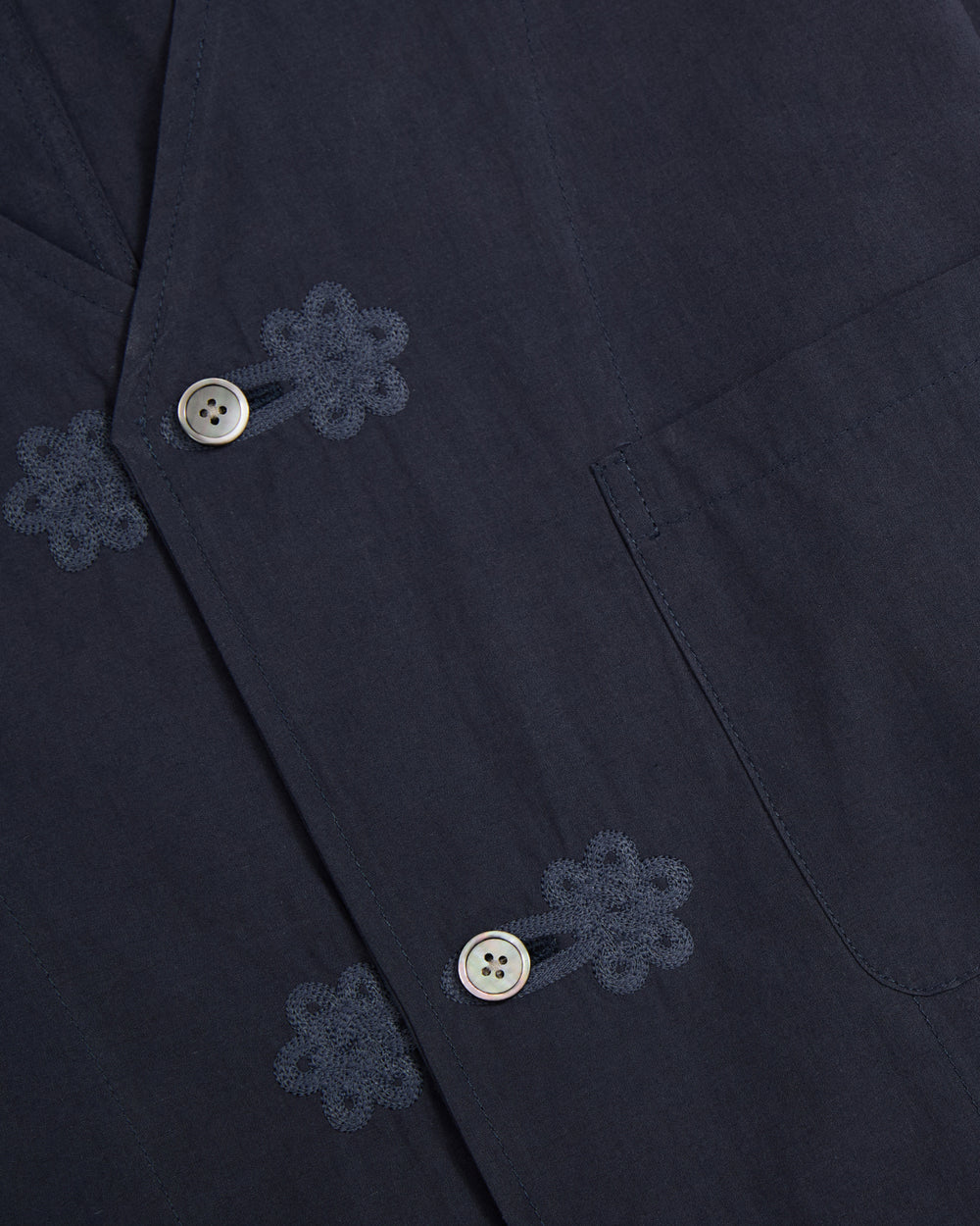Close-up of the Sundae School MAEHWA COLLARLESS SHIRT in dark blue, a unisex mid-layer featuring a pocket, light-colored buttons, and decorative Maehwa embroidery near the buttonholes.