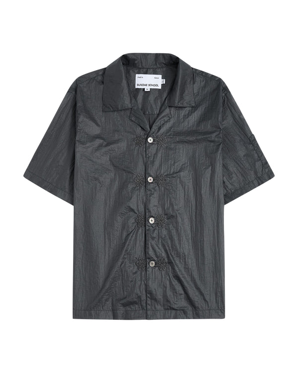 The MAEHWA EMBROIDERED SHEER SHIRT by Sundae School is a short-sleeve, dark gray, collared button-up featuring a crinkled texture and distinctive flower-shaped black buttons down the front—this unisex going-out shirt effortlessly elevates any look with its unique edge.