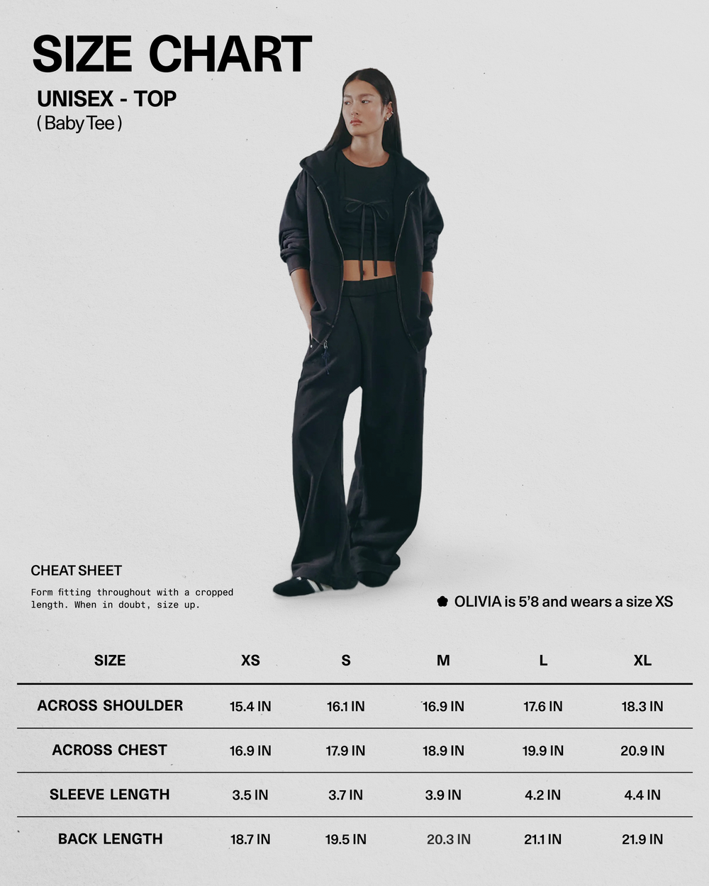 A woman wearing black pants, a BLACK TIE GORUM BABY TEE by Sundae School, and a black hoodie stands with hands in her pockets near a unisex size chart for tops, displaying XS-XL measurements for shoulders, chest, sleeves, and back.