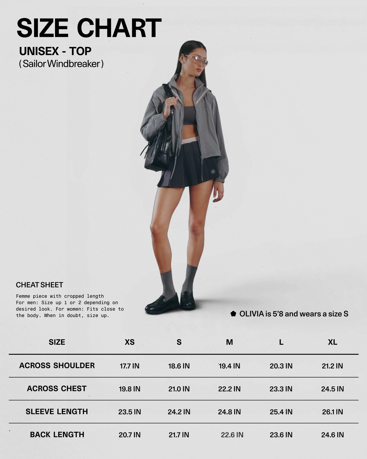 A person wearing the GREY SAILOR WINDBREAKER by Sundae School, styled with a black pleated skirt, socks, and boots, stands next to a unisex size chart for tops showing measurements from sizes S to XL. Text indicates the model is 5′8″ and wears a size S.
