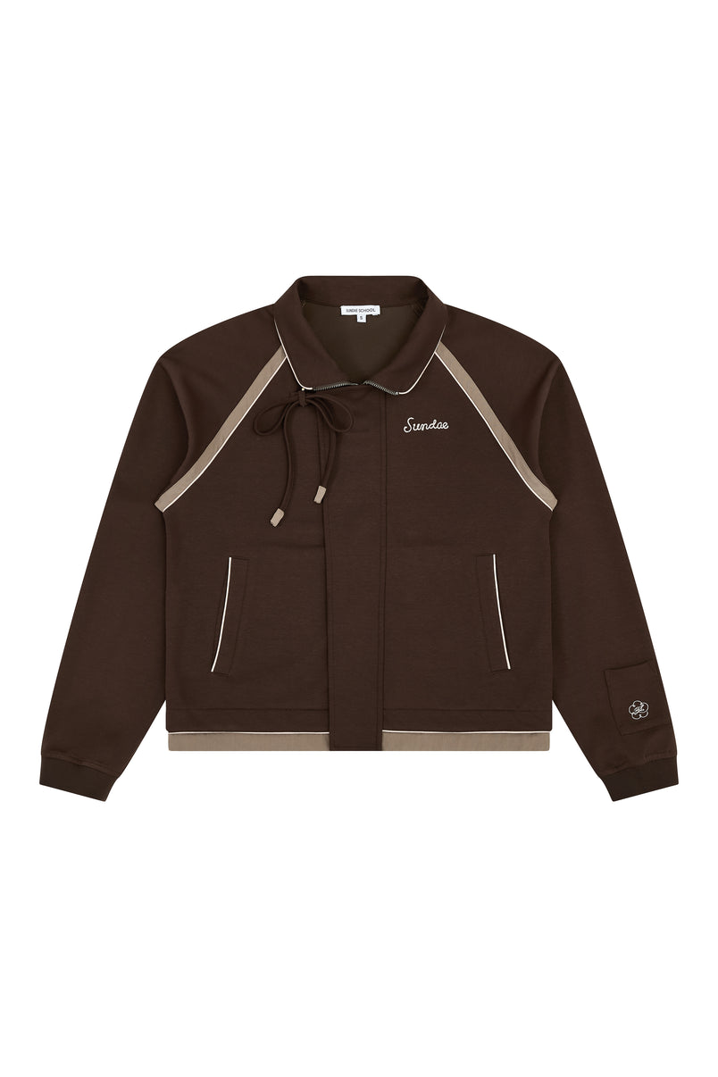 The BROWN PALISADE PARK TRACK JACKET by Sundae School is a brown zip-up athletic jacket featuring beige contrast fabric trim, front pockets, and a small embroidered logo on the left chest. It includes a collar with a tie and detailed chain-stitch embroidery on a patch near the left sleeve cuff.