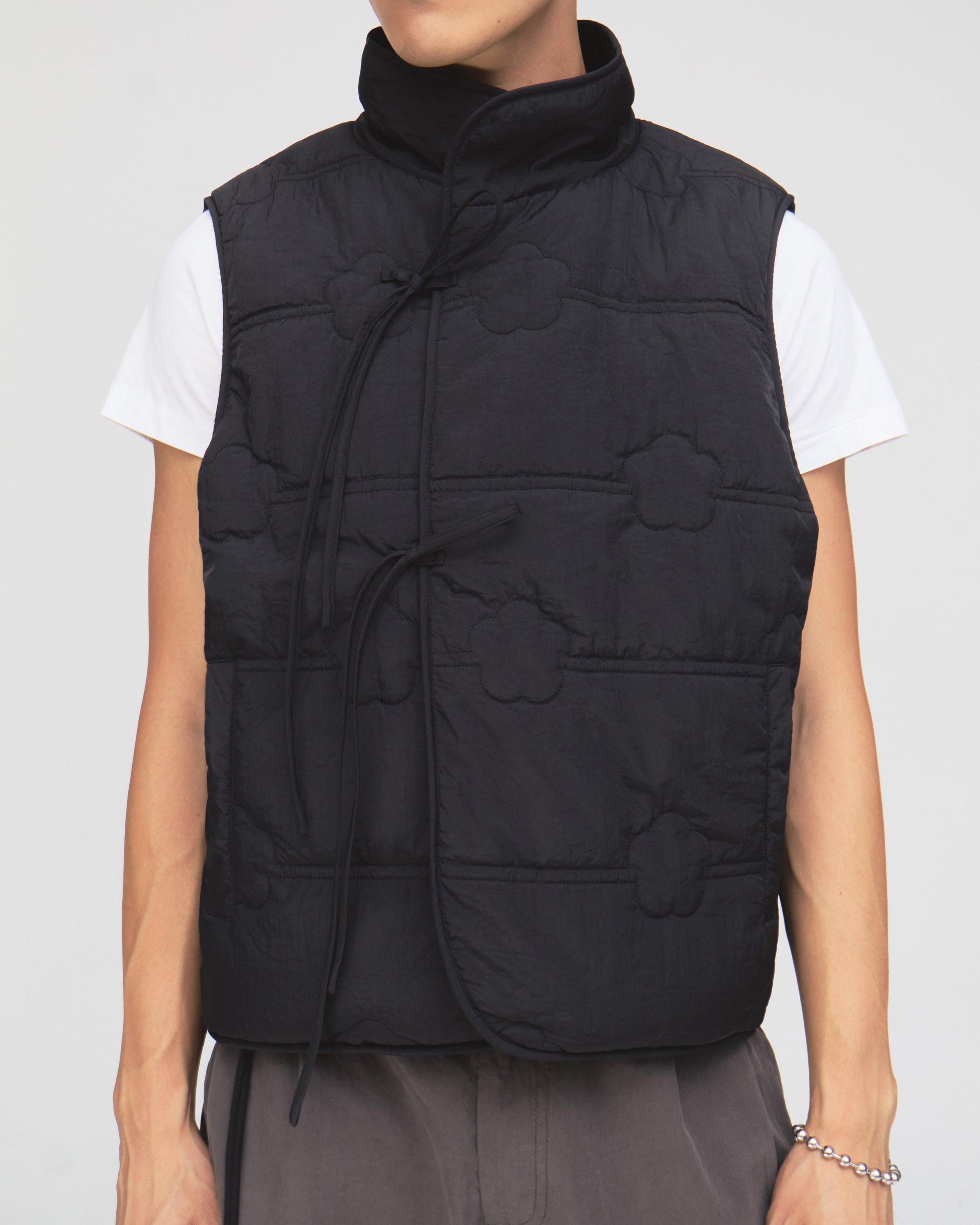 A person is wearing the BLACK MOMO REVERSIBLE FLEECE VEST by Sundae School over a white t-shirt and gray pants, standing against a plain background.