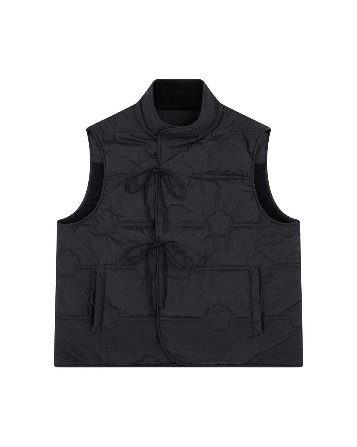 The BLACK MOMO REVERSIBLE FLEECE VEST by Sundae School is a sleeveless black quilted vest featuring a mandarin collar, front tie closures, large patch pockets, and a subtle floral stitching pattern. The vest is displayed laid flat on a white background.