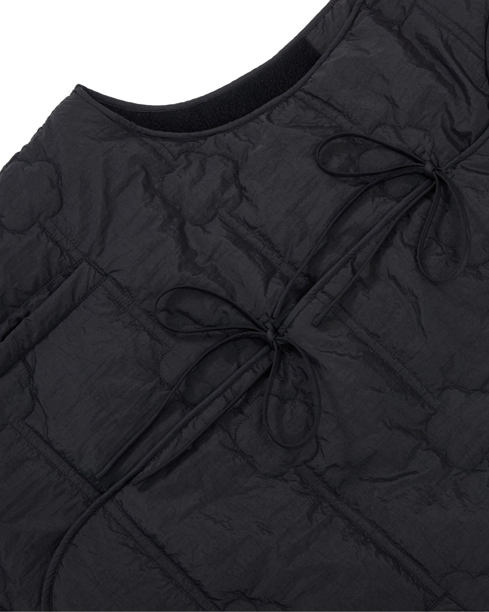 Close-up of the BLACK MOMO REVERSIBLE FLEECE VEST by Sundae School, featuring a black quilted design with two tied bows on the front and a curved neckline. The crinkled fabric showcases visible stitched patterns.