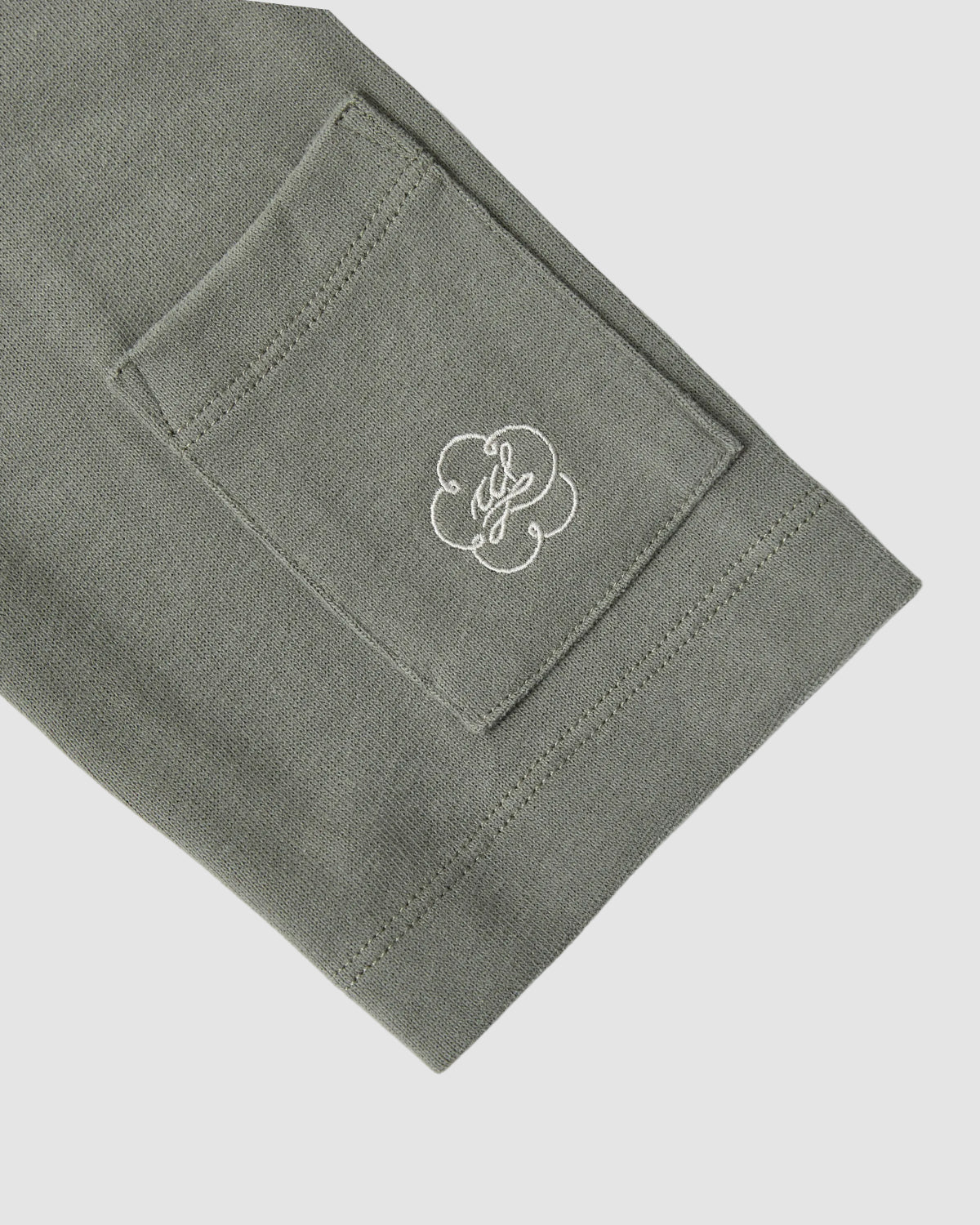 A close-up of the KHAKI OFFICE QUARTER ZIP by Sundae School shows its green cotton jersey sleeve, stash pocket, and a white embroidered cloud-like cursive haenyeo-inspired design on the pocket.