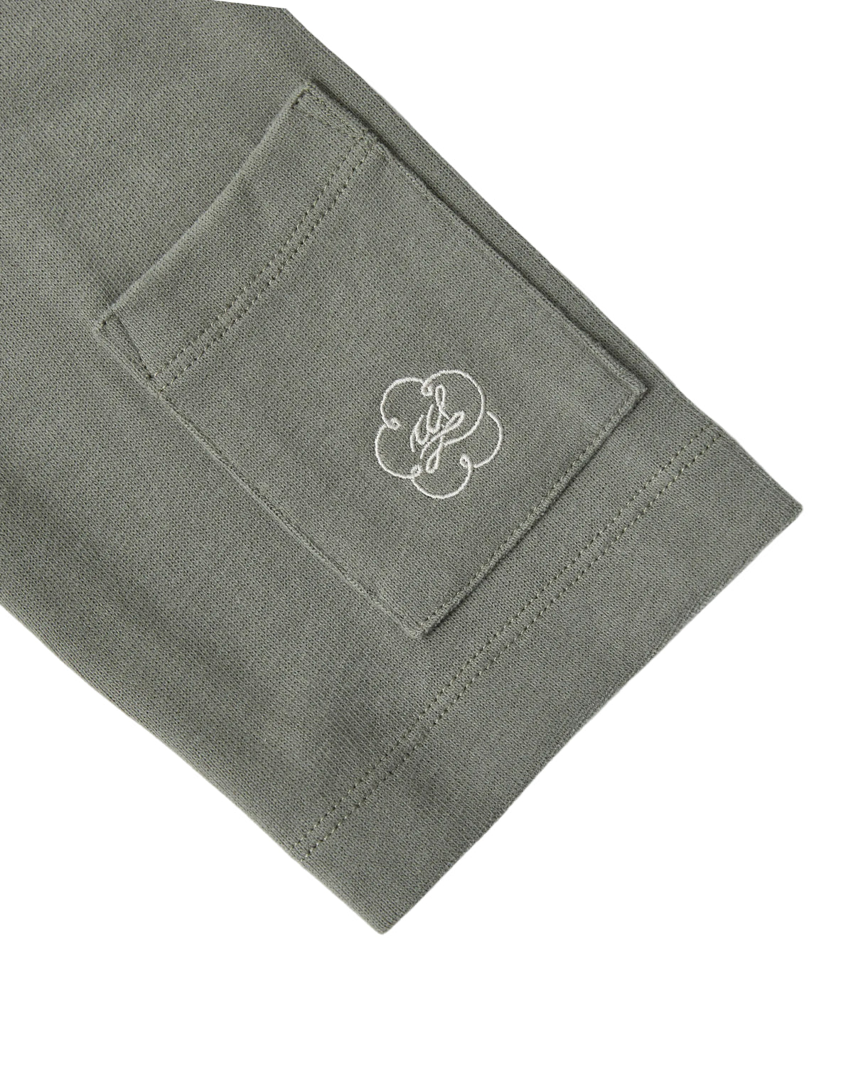 A close-up of the Sundae School KHAKI OFFICE QUARTER ZIP’s green cotton jersey sleeve, featuring a small rectangular stash pocket and a white embroidered logo with a decorative design.