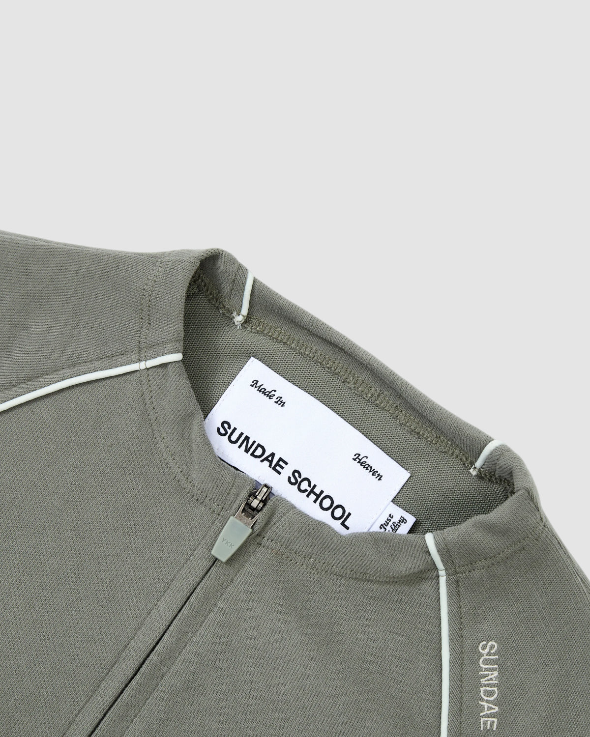 Close-up of the KHAKI OFFICE QUARTER ZIP by Sundae School. Gray quarter-zip features white shoulder piping, visible Sundae School label inside, and 