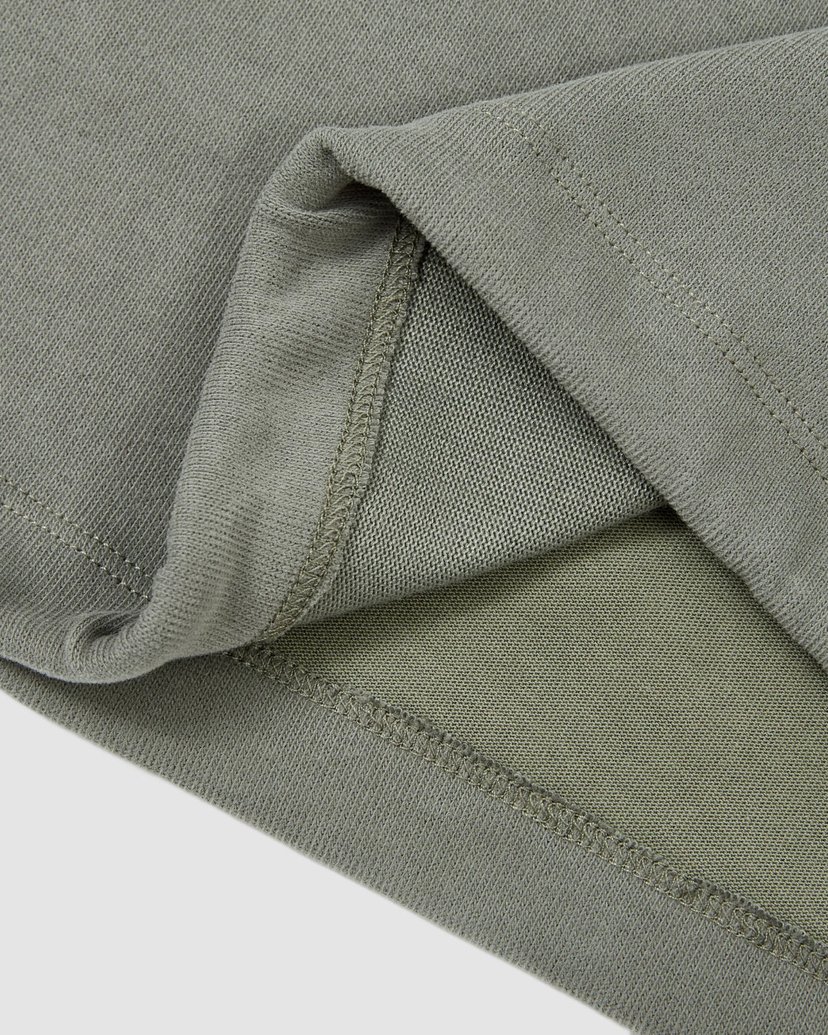 Close-up of the hem and inner seam of the Sundae School KHAKI OFFICE QUARTER ZIP, highlighting detailed stitching and the soft texture of its light olive green cotton jersey fabric.