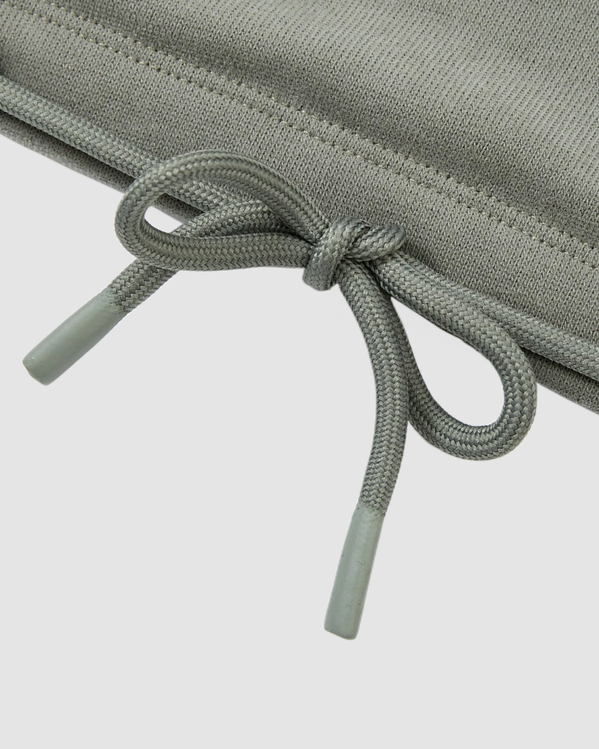 Close-up of a grey fabric drawstring with plastic tips, tied in a bow against a light background—details from Sundae School's KHAKI OFFICE QUARTER ZIP.