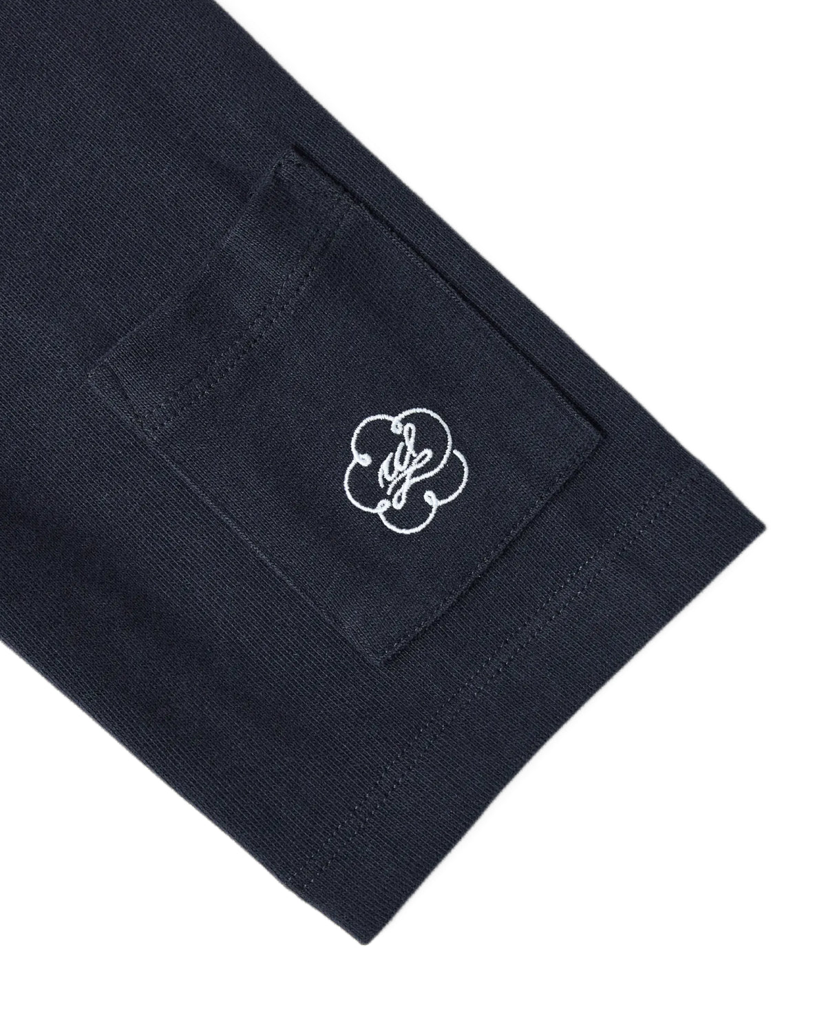 A close-up of the Sundae School NAVY OFFICE QUARTER ZIP’s dark navy cotton jersey sleeve, featuring a small stash pocket adorned with a white embroidered logo in an abstract flower or clover design.