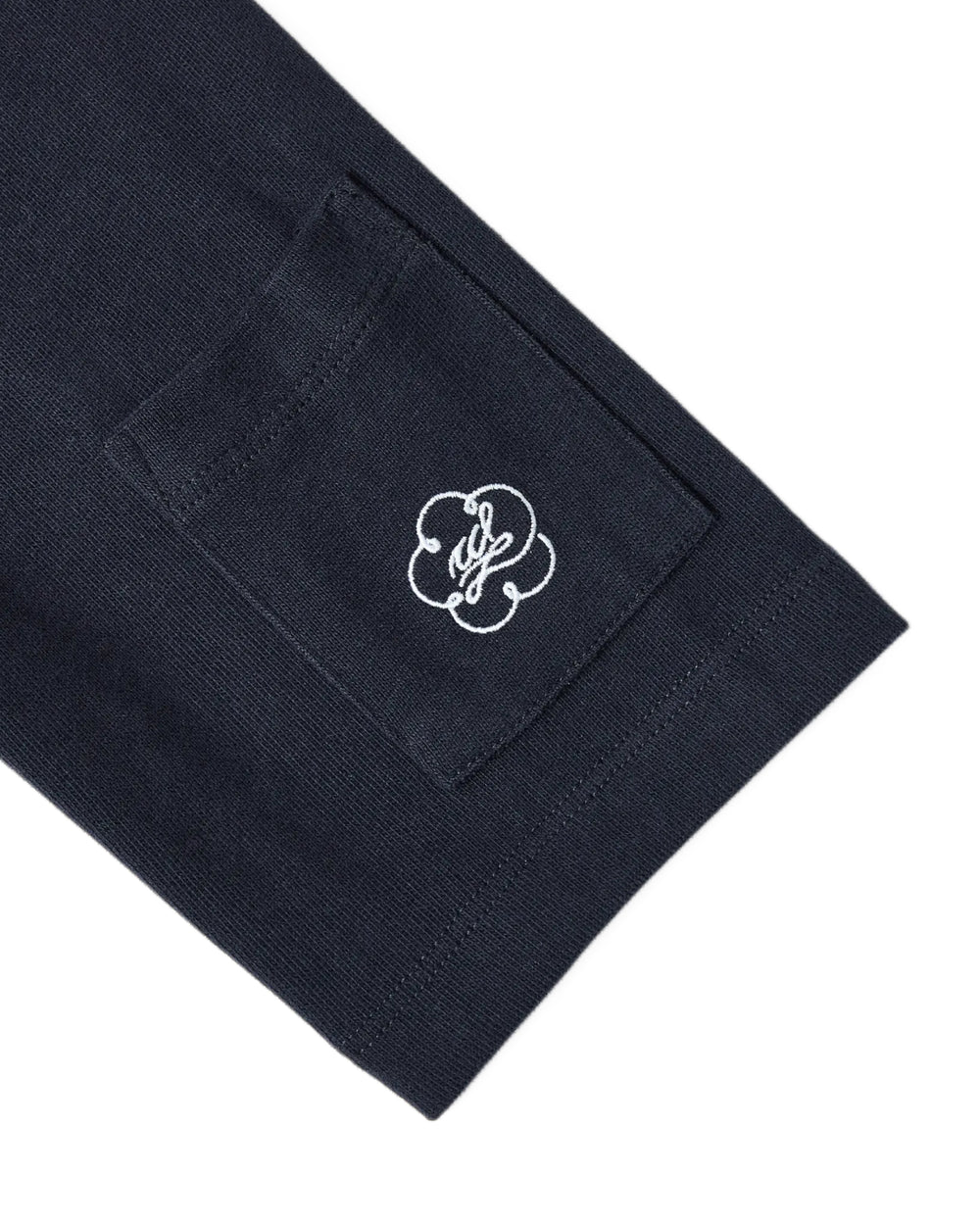A close-up of the Sundae School NAVY OFFICE QUARTER ZIP’s dark navy cotton jersey sleeve, featuring a small stash pocket adorned with a white embroidered logo in an abstract flower or clover design.