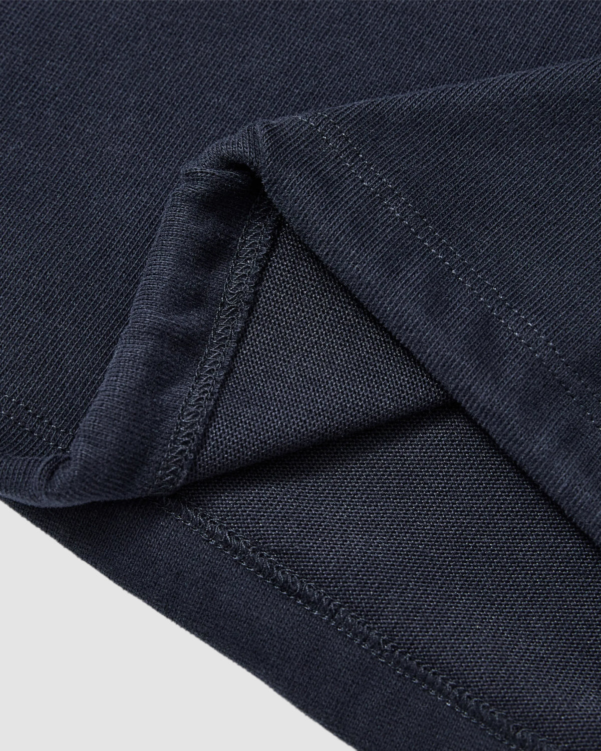 Close-up of the NAVY OFFICE QUARTER ZIP by Sundae School, highlighting the dark navy cotton jersey fabric with detailed stitching, texture, and hem against a light background.