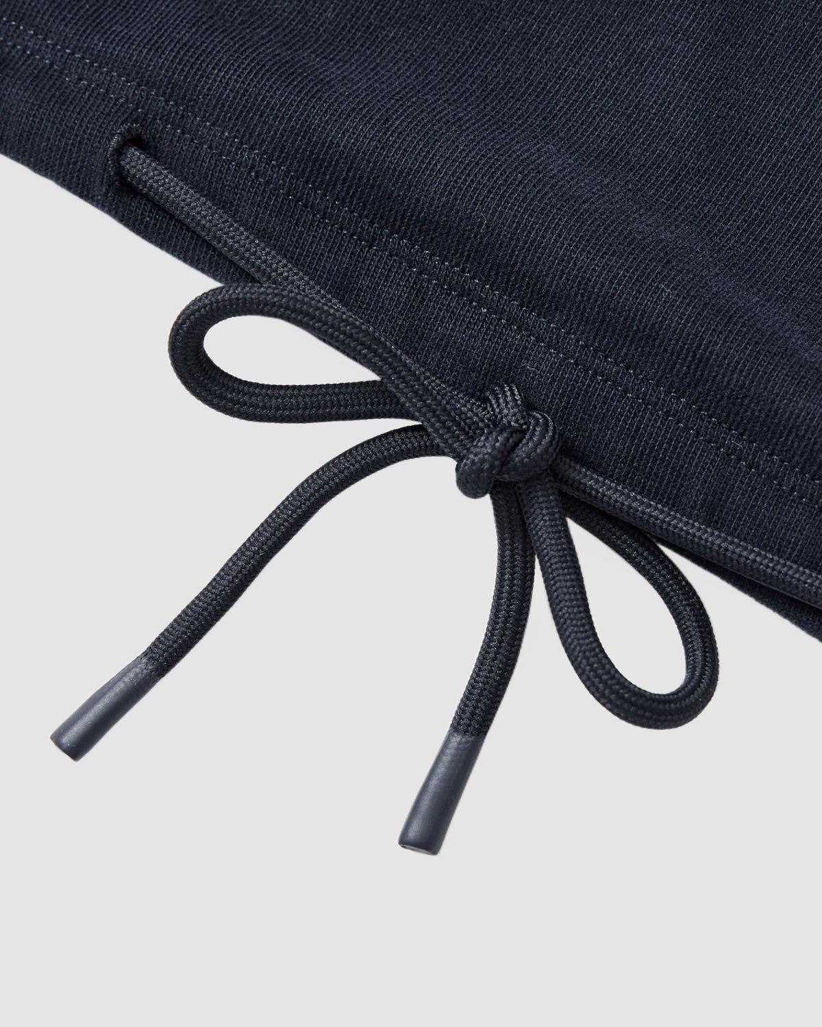 Close-up of the NAVY OFFICE QUARTER ZIP by Sundae School, showing a black drawstring tied in a bow with plastic tips on dark cotton jersey fabric, set against a plain light gray background.