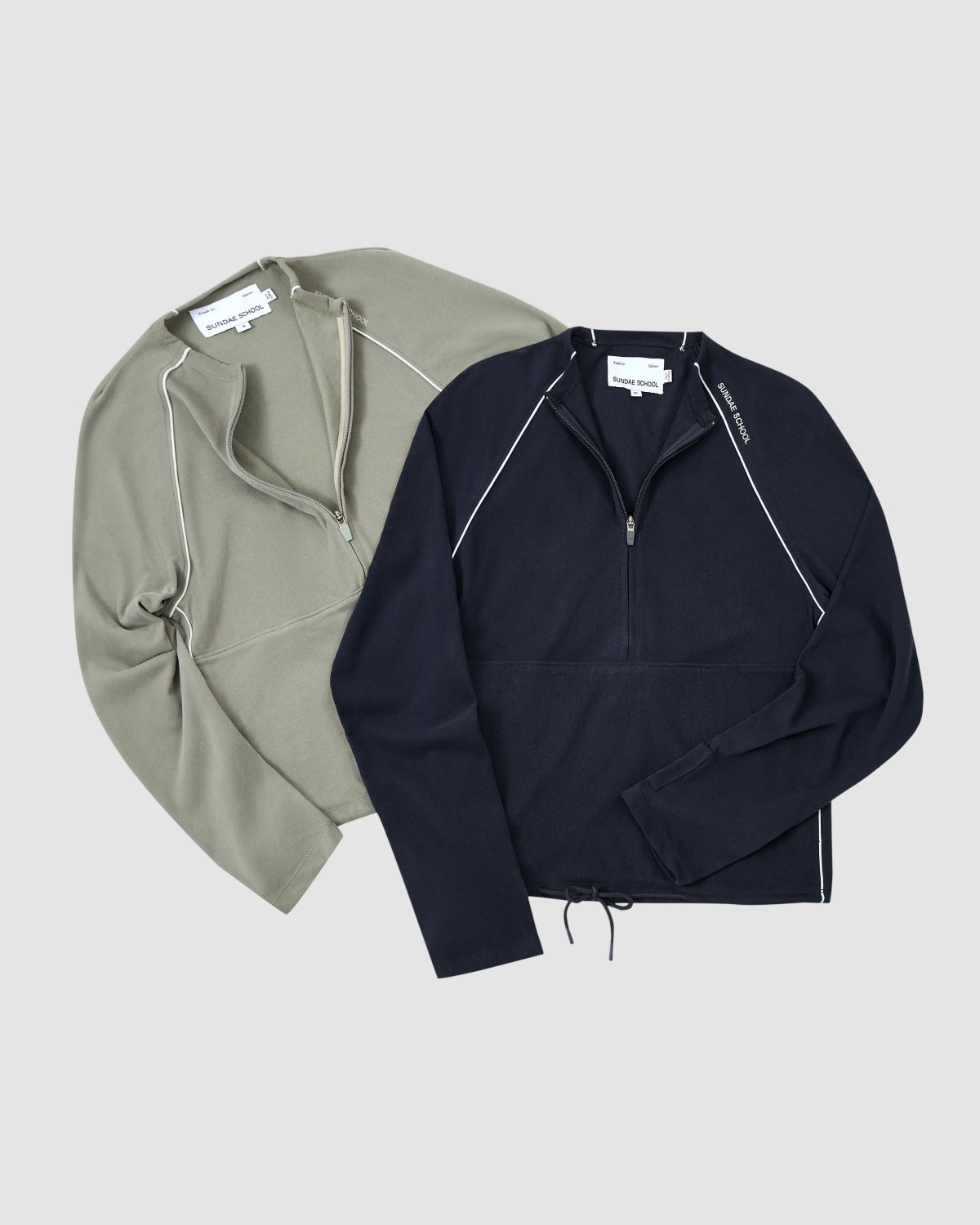 Two Sundae School KHAKI OFFICE QUARTER ZIP jackets with contrast stitching, one olive green and one black, both featuring a stash pocket, are laid flat side by side on a light gray background.
