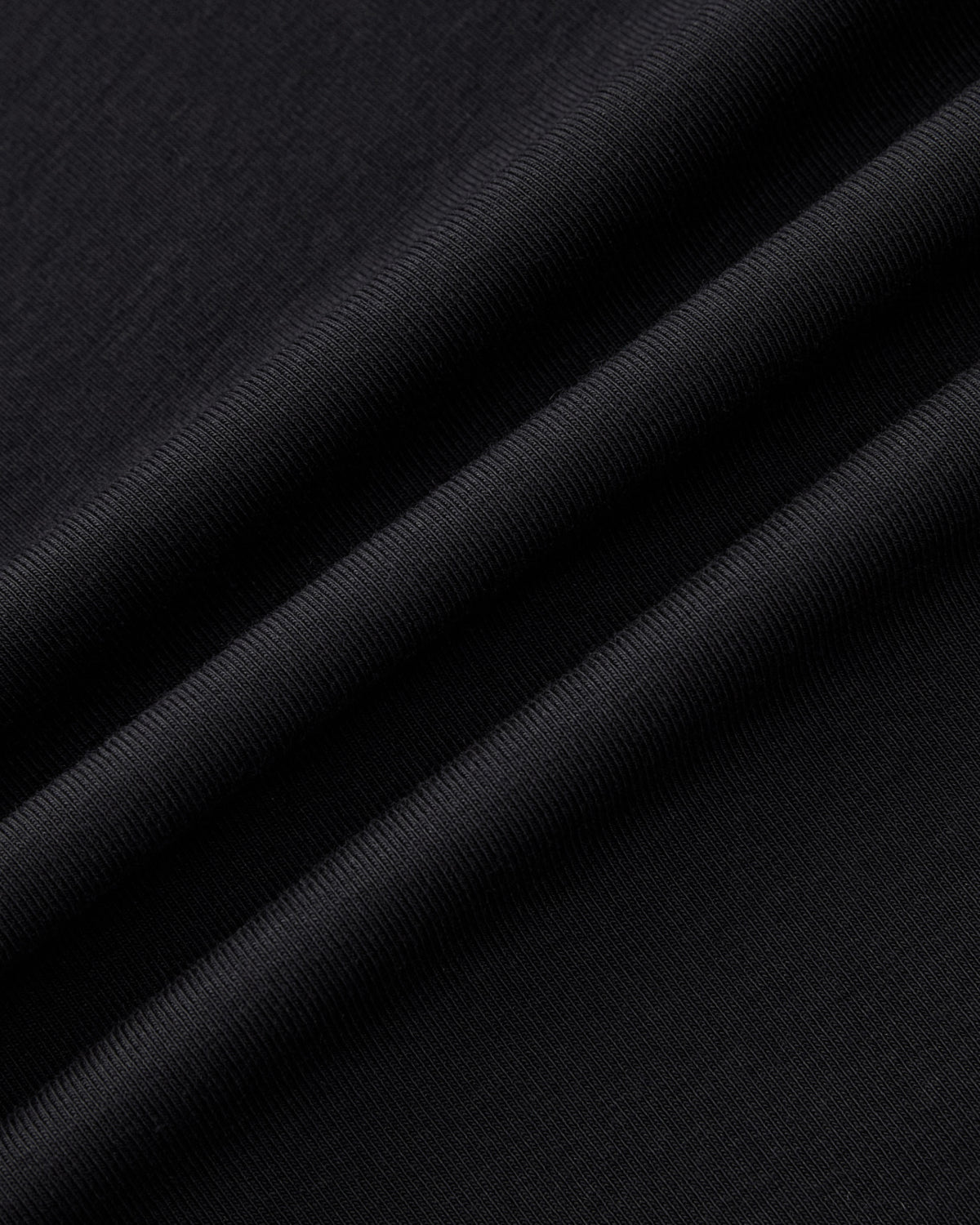 Close-up of the BLACK ORIGAMI GORUM TEE by Sundae School, featuring folded black fabric with visible texture and soft ridges that highlight its smooth and slightly ribbed surface.