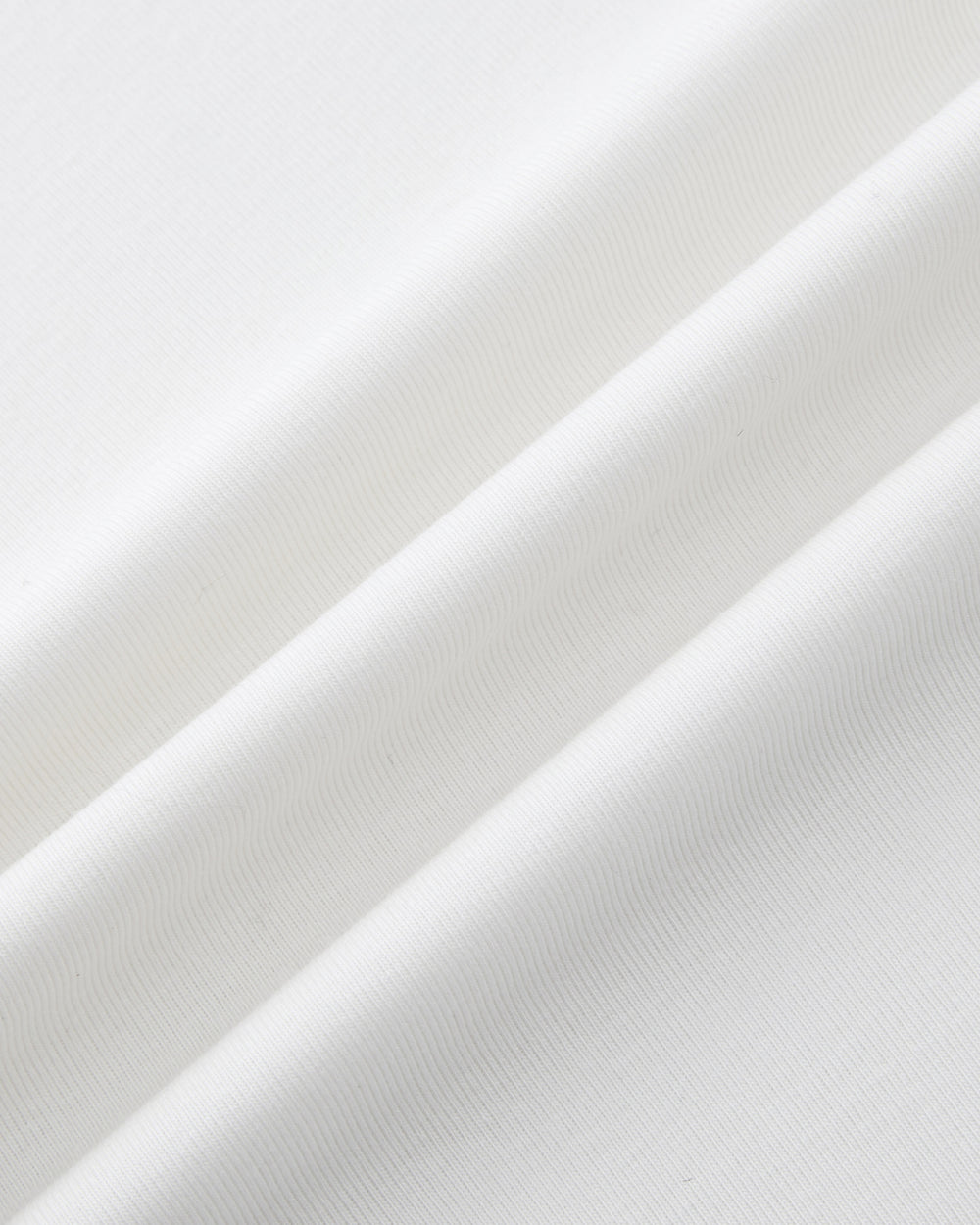 Close-up of the IVORY ORIGAMI GORUM TEE by Sundae School: features white fabric with a soft texture and subtle diagonal folds, revealing fine lines and gentle shadows.