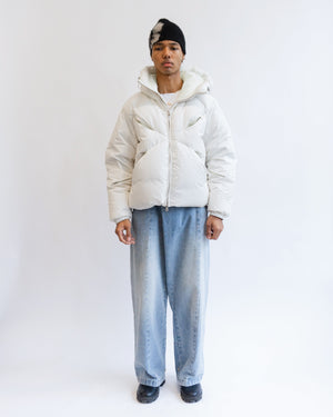 A person stands against a plain white background wearing the Sundae School IVORY LIME ORIGAMI PUFFER, wide-leg light blue jeans, black shoes, and a black beanie with a white patch.