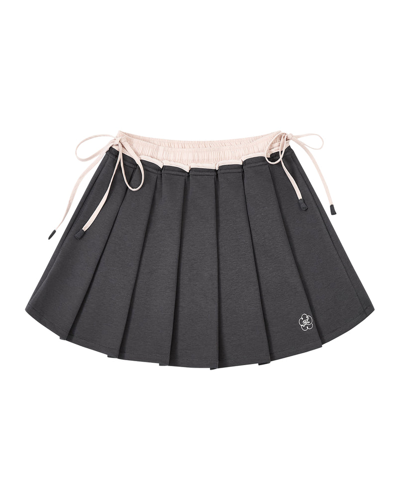 CHARCOAL PLEATED JERSEY MINI SKIRT by Sundae School: A charcoal gray knife-pleated mini skirt with a light pink waistband and matching drawstrings, finished with a small white embroidered flower logo near the hem.