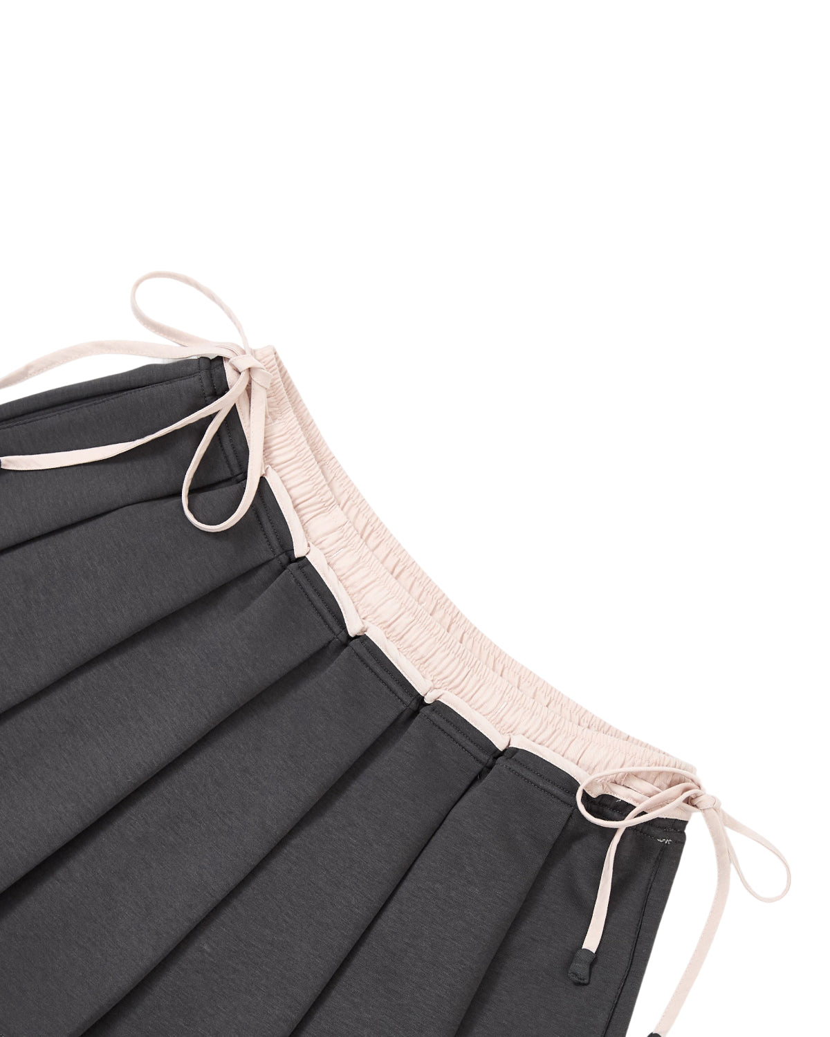 The CHARCOAL PLEATED JERSEY MINI SKIRT by Sundae School is a dark knife-pleated mini skirt featuring a light beige elastic waistband and matching beige drawstrings. Shown from an angled top-down view on a white background, this schoolgirl-inspired mini skirt is crafted from a comfortable cotton blend jersey for everyday wear.