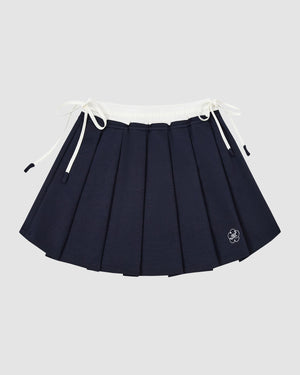 The NAVY PLEATED JERSEY MINI SKIRT by Sundae School features a white elastic waistband, drawstring ties on both sides, and a small embroidered flower near the hem, shown against a plain light gray background.