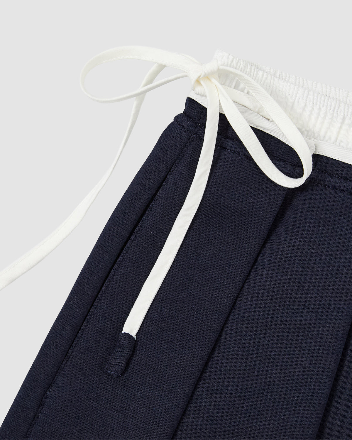 Close-up of Sundae School's NAVY PLEATED JERSEY MINI SKIRT styled next to navy blue pants with an elastic waistband and white drawstrings, set against a light gray background.
