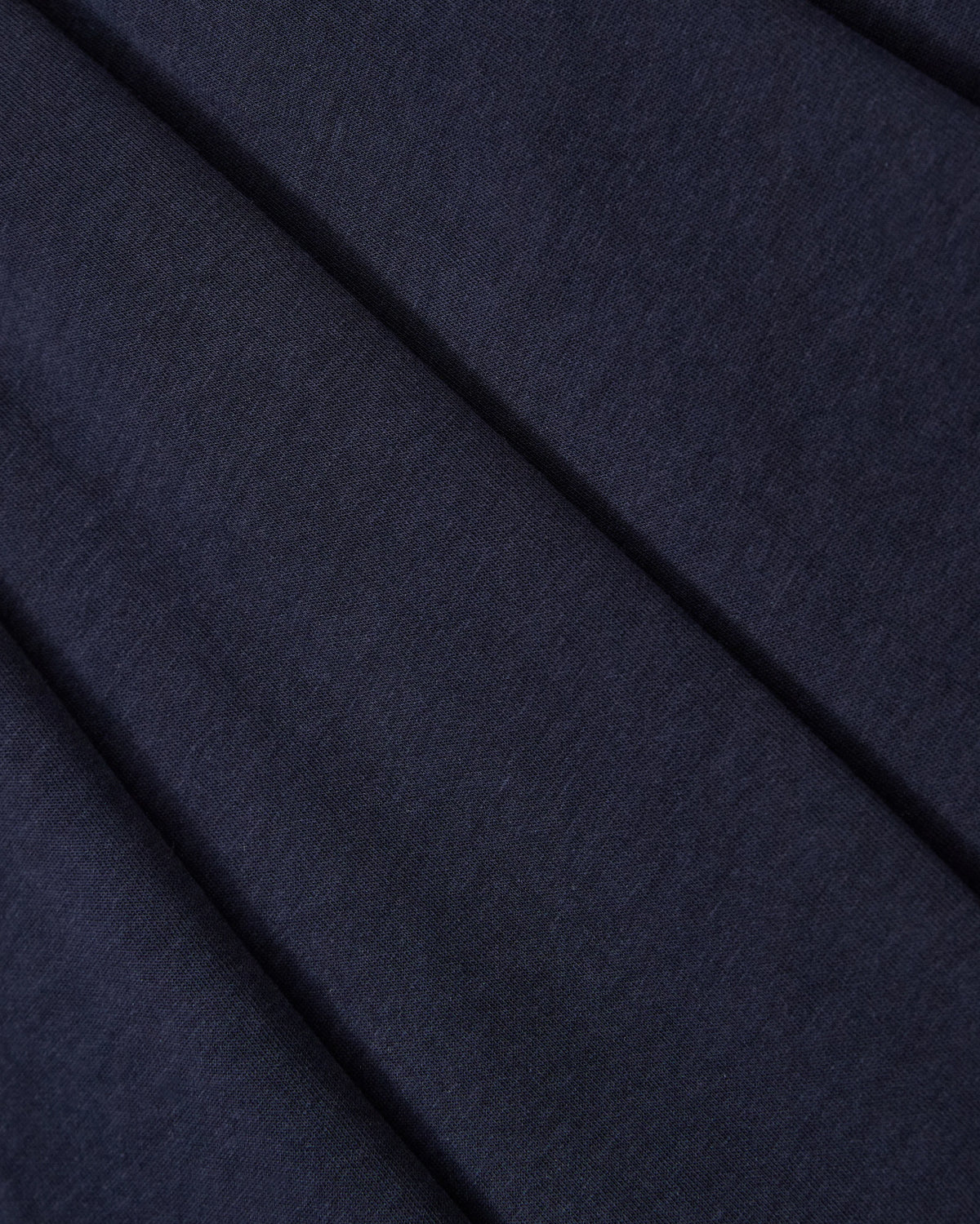 Close-up of Sundae School's NAVY PLEATED JERSEY MINI SKIRT: dark navy fabric with a soft texture and visible weaves, arranged in gentle diagonal folds for added depth.