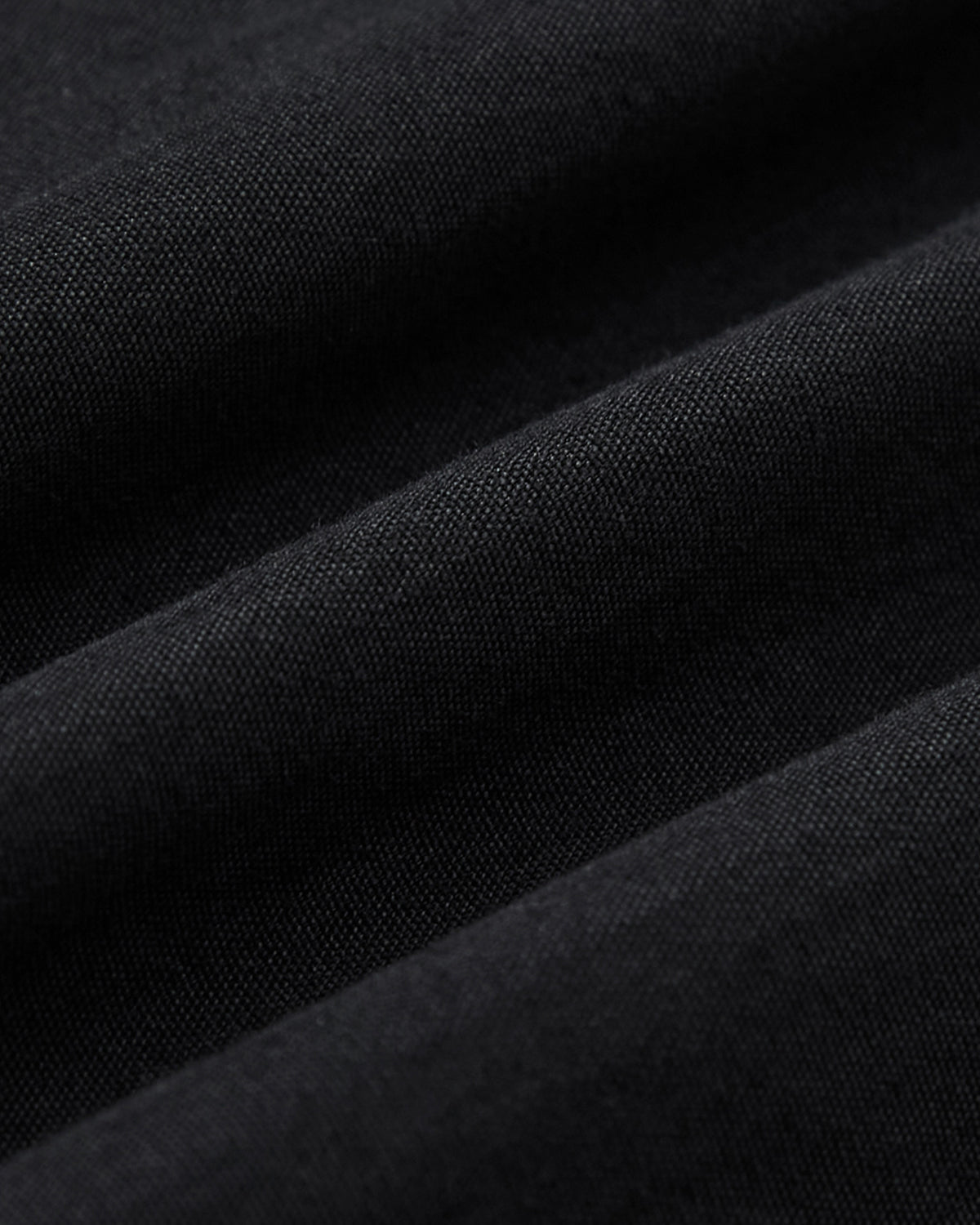 Close-up of black fabric with visible texture and soft folds, highlighting fine woven fibers and gentle shadows—ideal for Sundae School’s BLACK PLEATED PALAZZO PANTS.