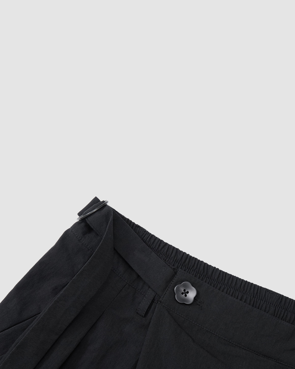 Close-up of the waistband on Sundae School’s BLACK PLEATED PALAZZO PANTS, showing the asymmetric fly, mochi button detail, belt loop, and adjustable side buckle against a plain light gray background.