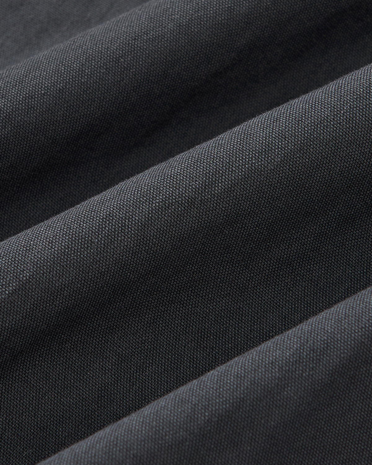 Close-up of textured dark gray fabric in soft folds from Sundae School's CHARCOAL PLEATED UNIFORM SLACKS, perfect for versatile unisex wear.