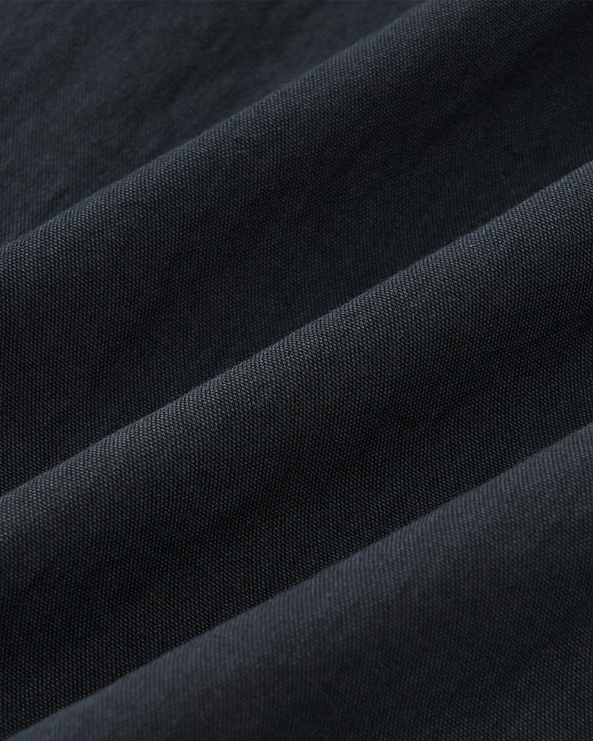Close-up of Sundae School’s NAVY PLEATED UNIFORM SLACKS shows smooth, fine dark fabric with diagonal folds. The soft, slightly matte material creates subtle shadows and highlights along each crease.