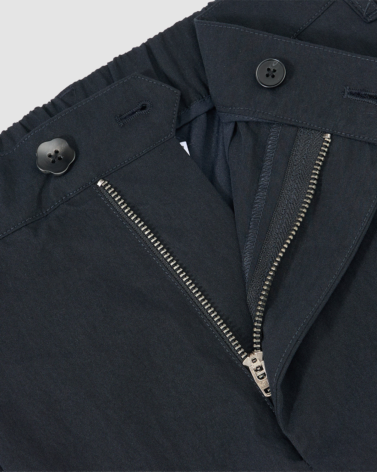 Close-up of Sundae School's NAVY PLEATED UNIFORM SLACKS, showing an open zipper fly and two black buttons on the waistband against a light background.