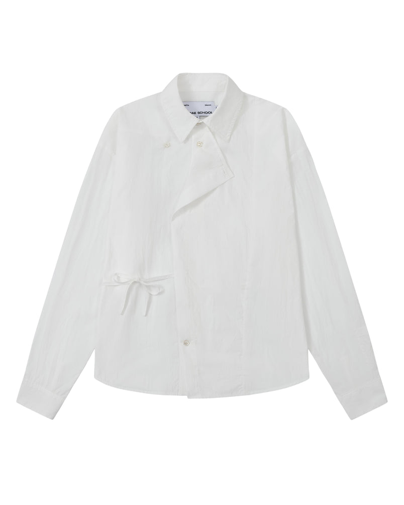 The WHITE POPLIN TIE GORUM SHIRT by Sundae School is a unisex, tailored-fit white long-sleeve shirt crafted from cotton nylon poplin. It features an asymmetrical front, classic collar, and distinctive side tie detail, with a double-layered front panel adding dimension. Shown on a plain background.