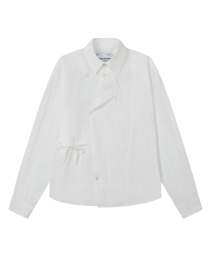 A front flat-lay view of an off-white long-sleeve button-up shirt crafted from textured crinkle fabric. It features an asymmetrical wrap-front construction with a side waist tie, a pointed collar, and flower-shaped button details.