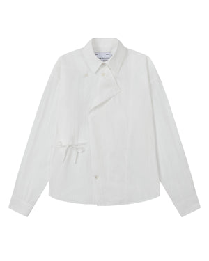 A front flat-lay view of an off-white long-sleeve button-up shirt crafted from textured crinkle fabric. It features an asymmetrical wrap-front construction with a side waist tie, a pointed collar, and flower-shaped button details.