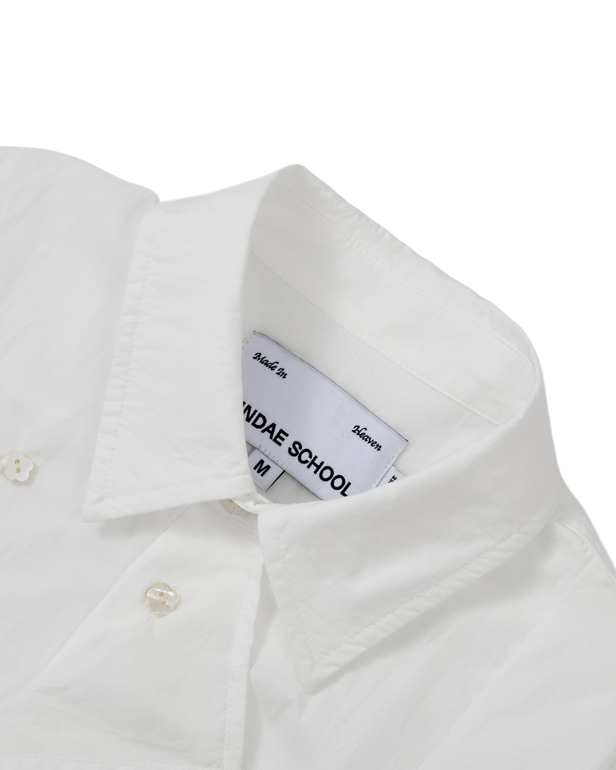 A close-up of the WHITE POPLIN TIE GORUM SHIRT by Sundae School highlights the structured double-layered front panel, placket, and buttons. Crafted from white cotton nylon poplin, this unisex tailored shirt features a visible inner Sundae School label and is neatly pressed against a plain white background for a crisp presentation.