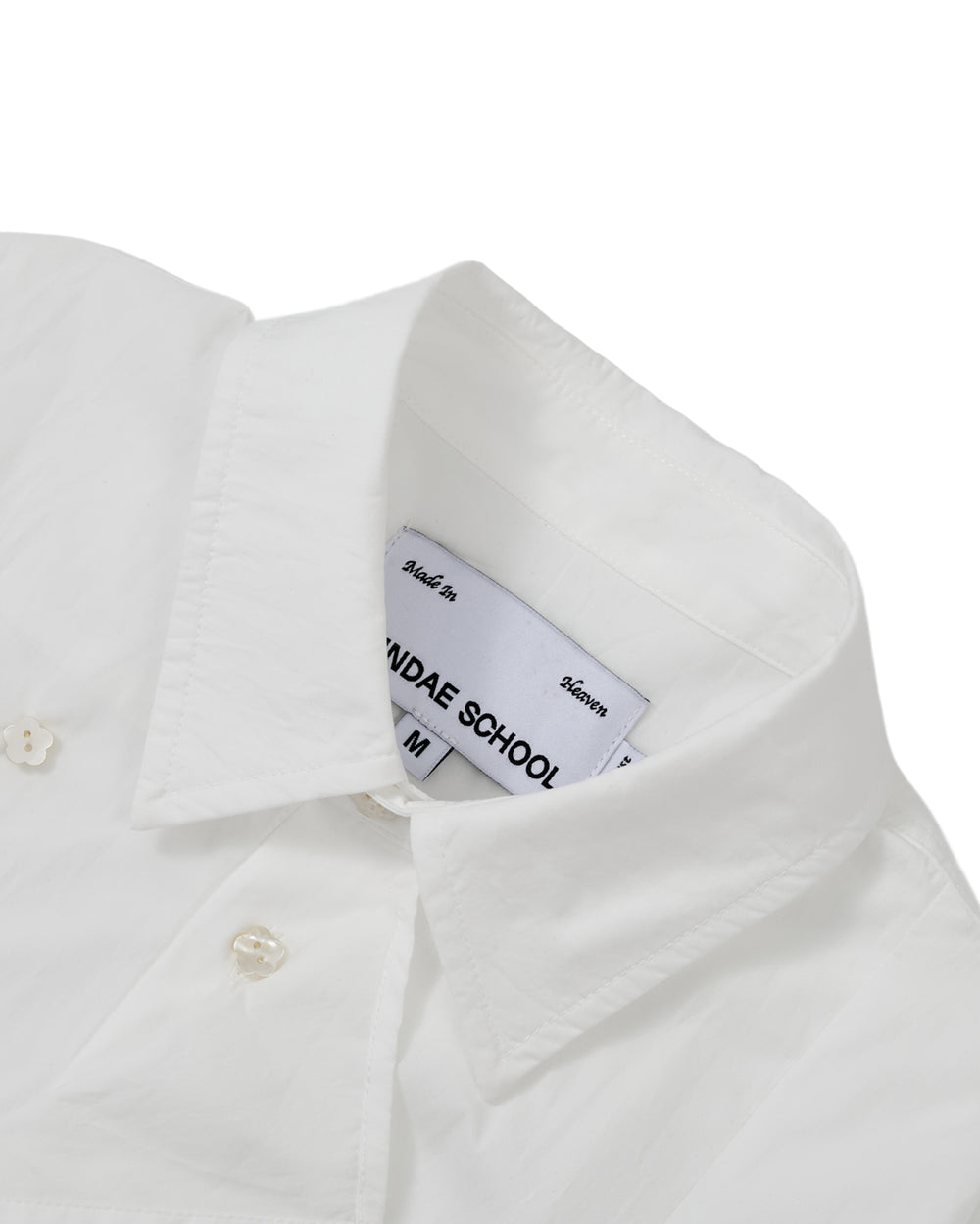 A close-up of the WHITE POPLIN TIE GORUM SHIRT by Sundae School highlights the structured double-layered front panel, placket, and buttons. Crafted from white cotton nylon poplin, this unisex tailored shirt features a visible inner Sundae School label and is neatly pressed against a plain white background for a crisp presentation.