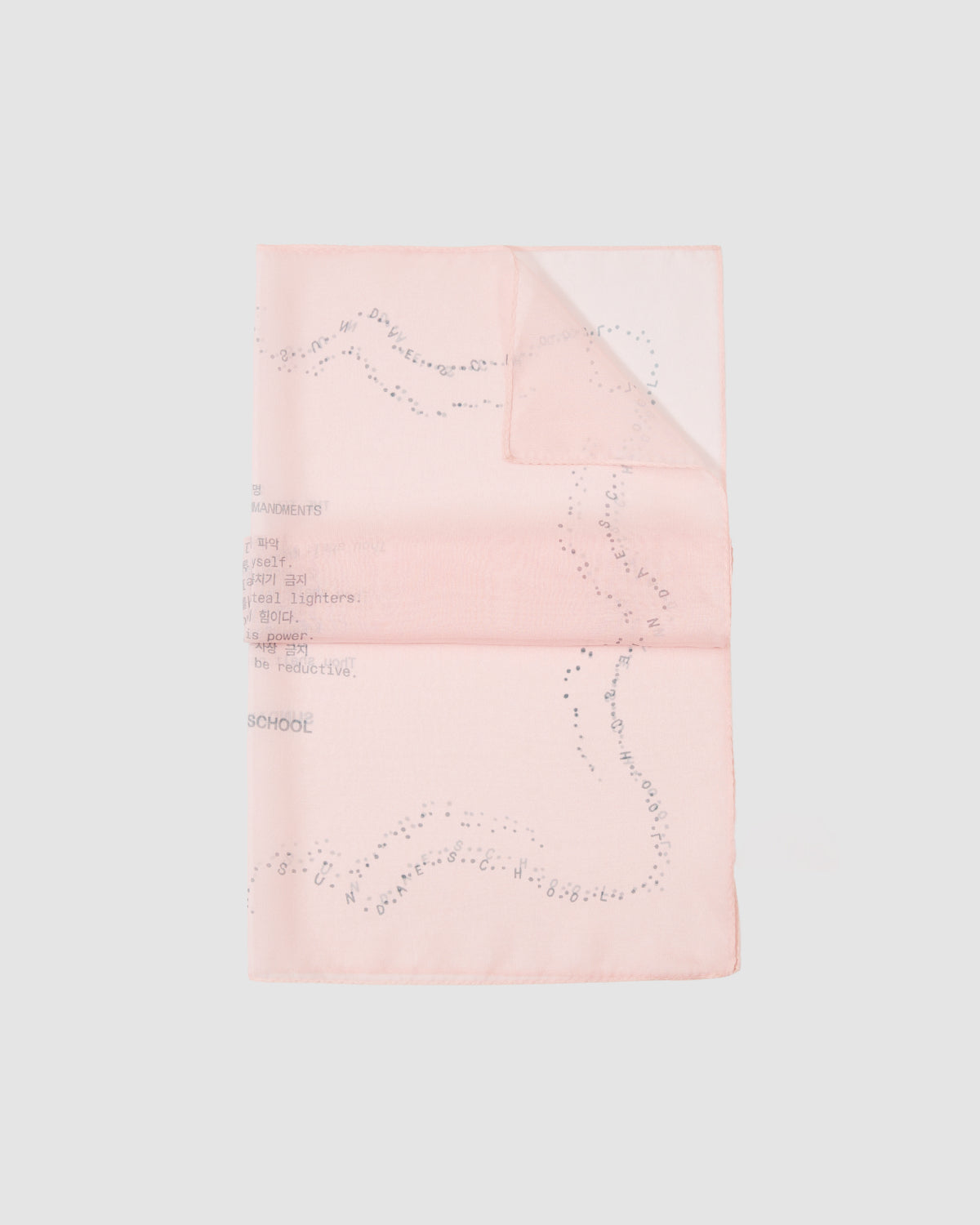 The Sundae School BABY PINK 10 COMMANDMENTS ORGANZA BANDANA is shown flat on a plain grey background with the upper right corner folded, revealing its light pink silk organza fabric adorned with faint text and dotted patterns.