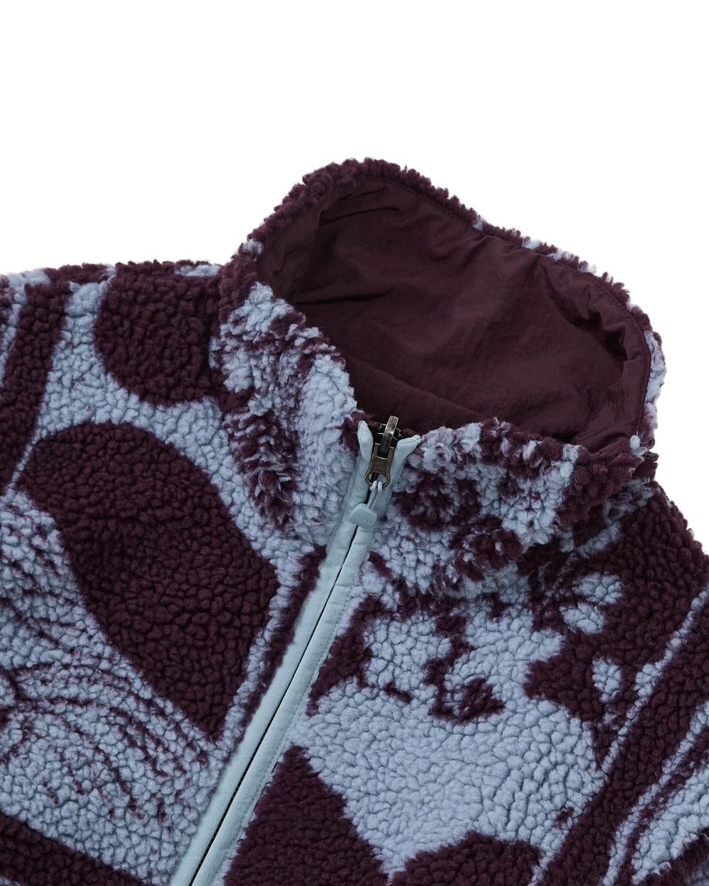 Close-up of the Sundae School PLUM REVERSIBLE GOSTOP FLEECE, featuring a partially unzipped stand collar and soft, textured sherpa fabric in a purple and light blue abstract pattern.