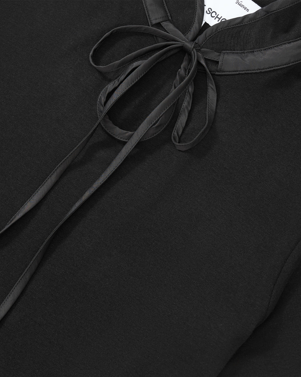 Close-up of the BLACK RIBBON TIE POLO by Sundae School, a black shirt featuring a shiny ribbon tie at the collar, elegantly tied into a bow. The collar and bow showcase a satin-like texture that contrasts with the shirt’s matte fabric. This design subtly references traditional Korean goreum style while blending modern sophistication.