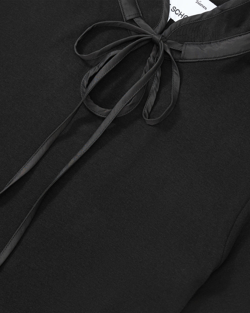 Close-up of the BLACK RIBBON TIE POLO by Sundae School, a black shirt featuring a shiny ribbon tie at the collar, elegantly tied into a bow. The collar and bow showcase a satin-like texture that contrasts with the shirt’s matte fabric. This design subtly references traditional Korean goreum style while blending modern sophistication.