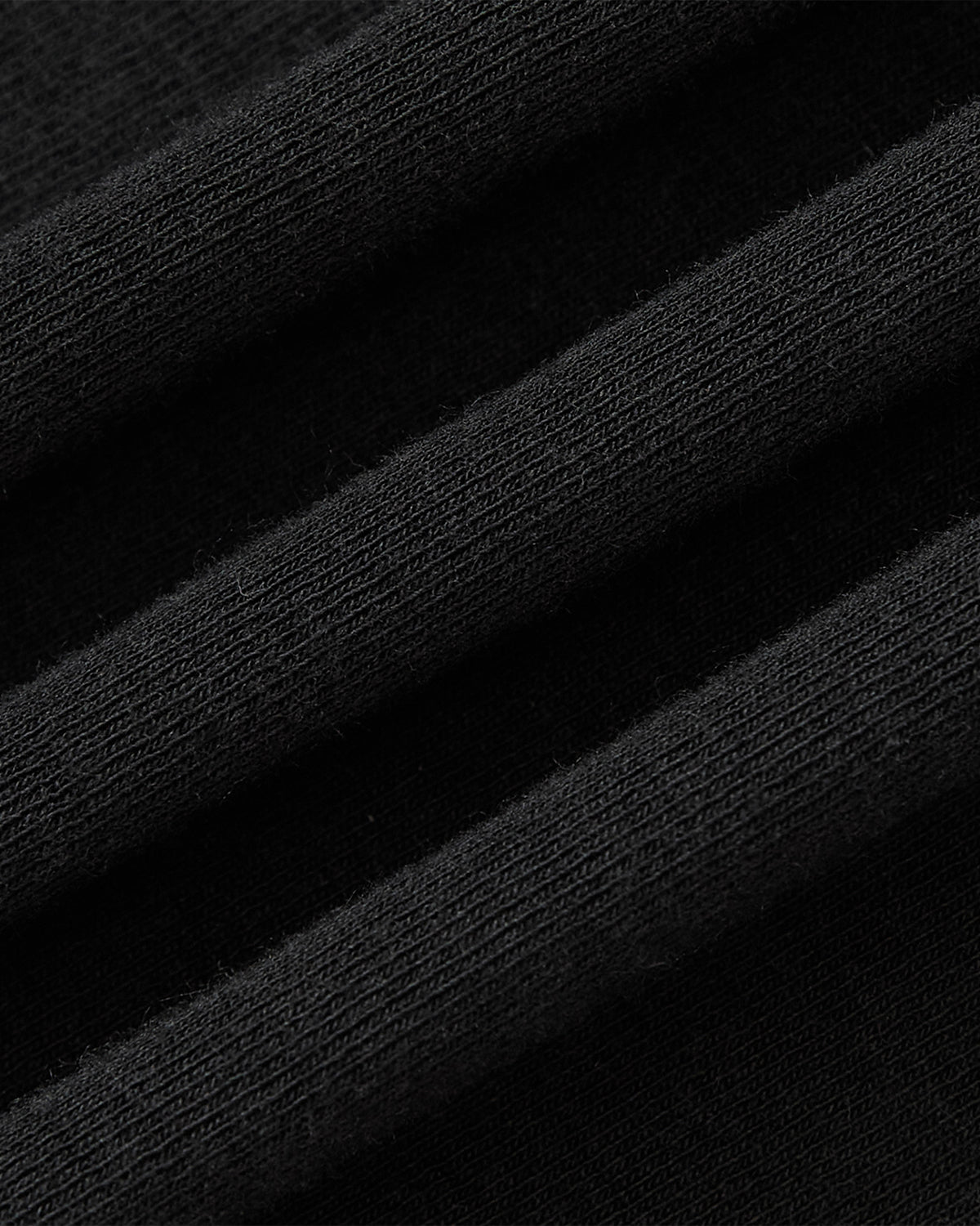 Close-up of black, ribbed fabric with a soft texture and fine knit patterns highlights the subtle elegance of the Sundae School BLACK RIBBON TIE POLO’s teardrop collar.