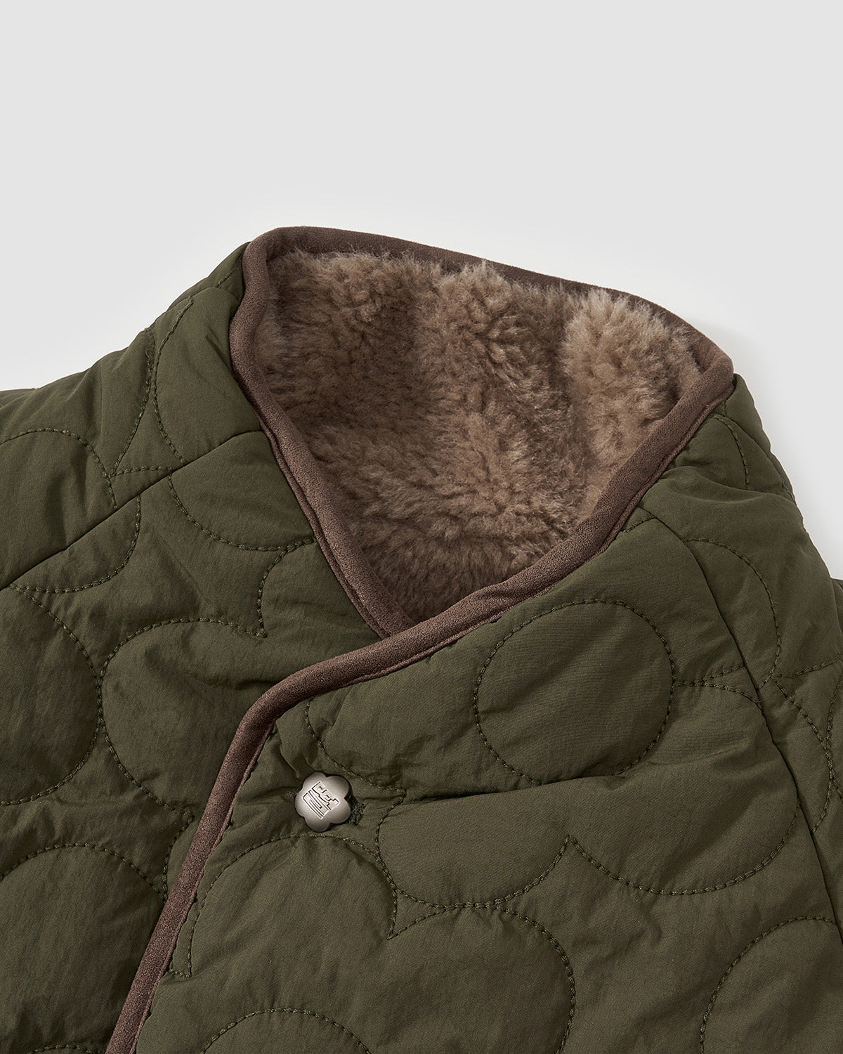 Close-up detail of the Reversible Flower Quilted Jeogori Fleece collar showing brown sherpa fleece lining and circular quilted pattern with a brown button closure.