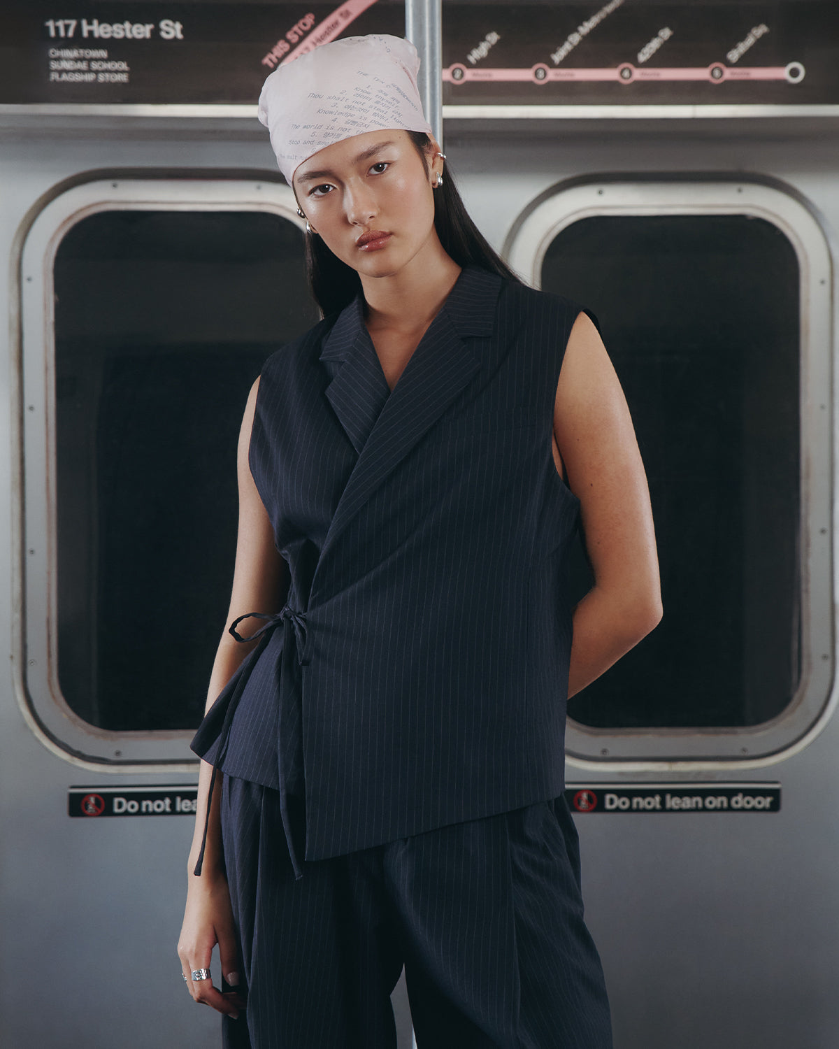 A person wearing the SABRINA VEST by Sundae School stands in a subway car, with “117 Hester St” and a subway map in the background.