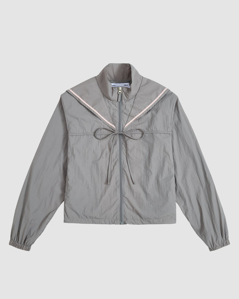 The CHARCOAL SAILOR WINDBREAKER by Sundae School is a light gray cropped jacket with a sailor collar, pink trim, front tie, and long sleeves with elastic cuffs, shown against a plain white background.