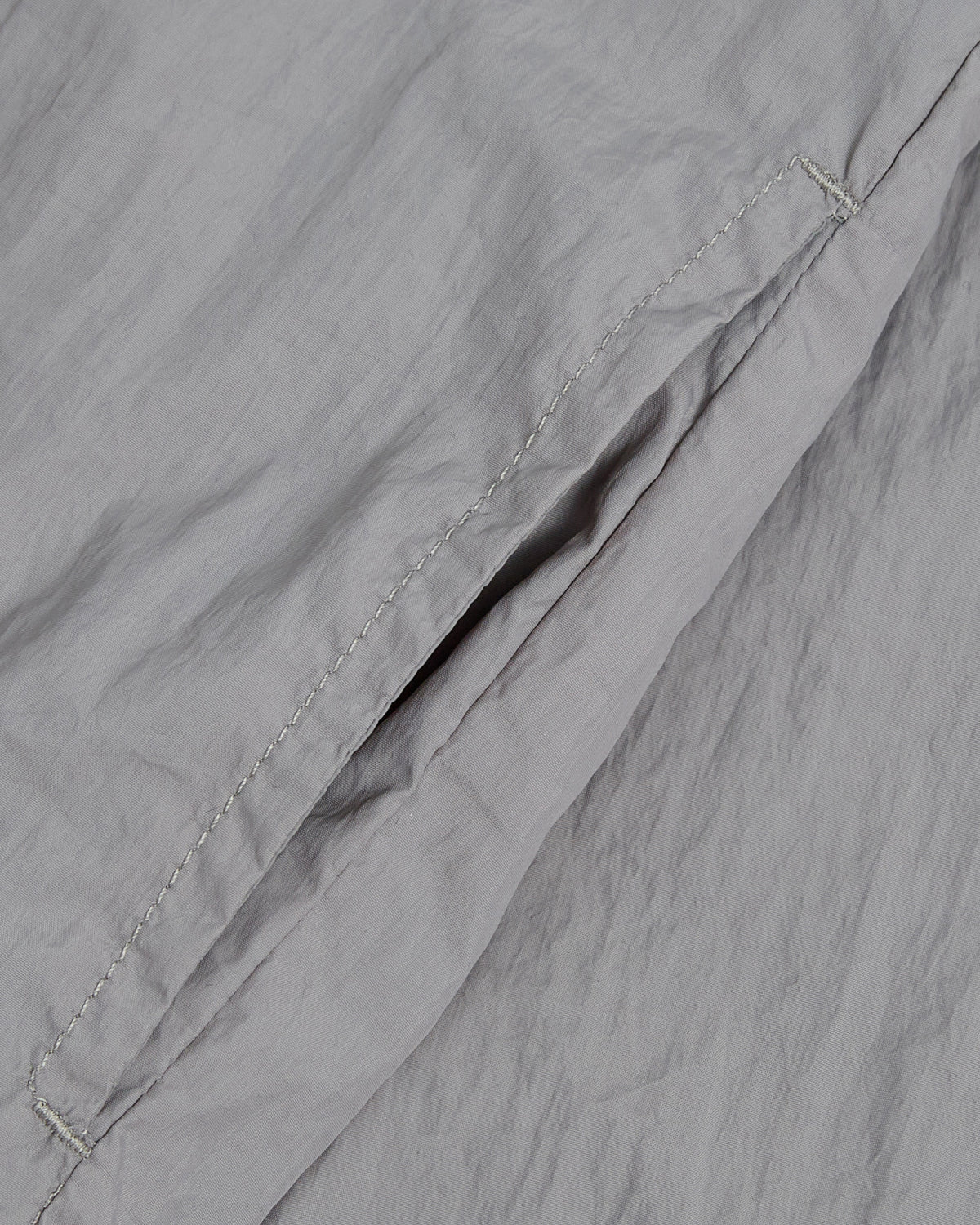 Close-up of Sundae School's CHARCOAL SAILOR WINDBREAKER—light gray with a side pocket and visible seams. The slightly crinkled fabric evokes its lightweight, breezy feel, embodying the UV protection style of this jacket.