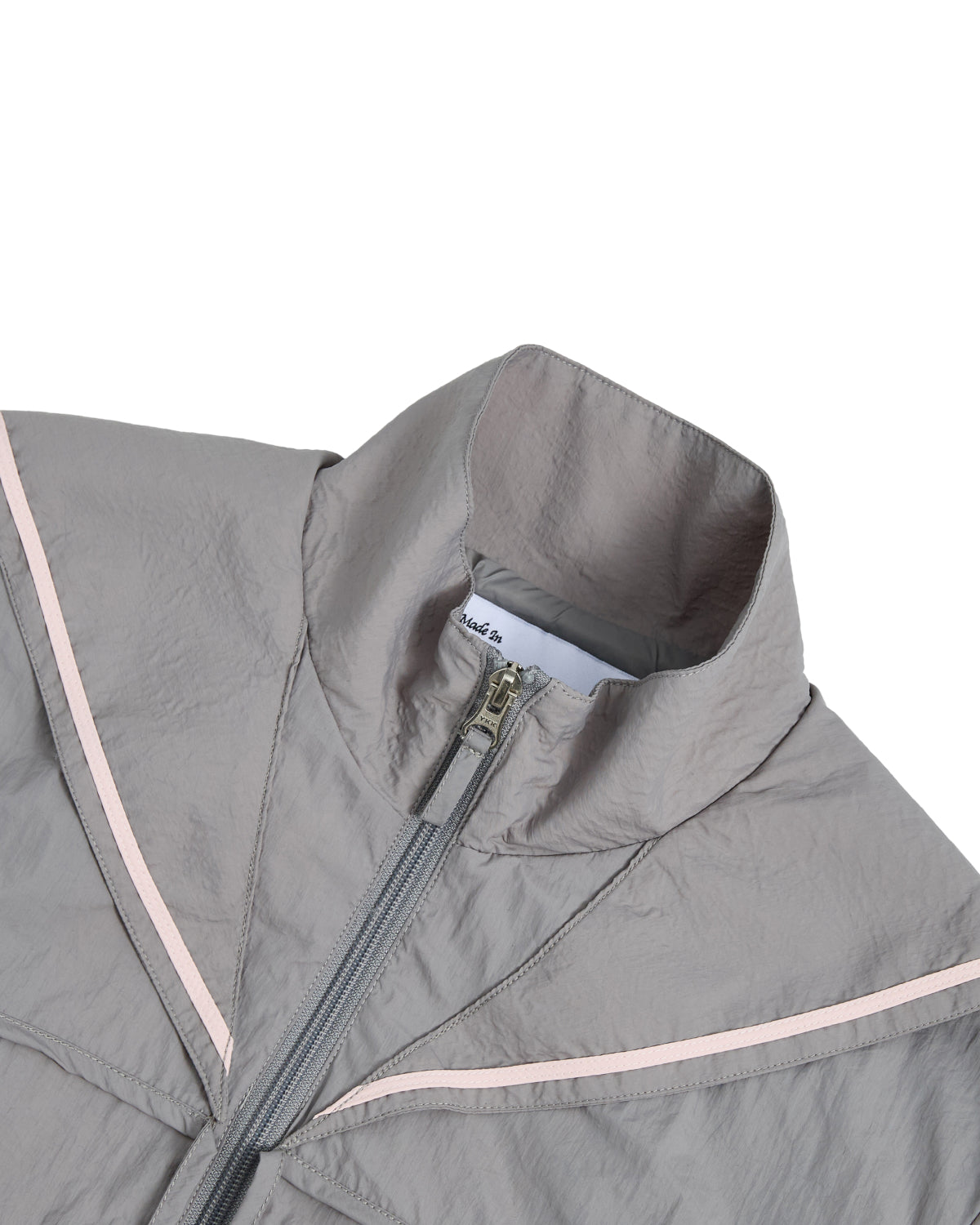The GREY SAILOR WINDBREAKER by Sundae School is a light gray cropped jacket featuring a high collar, partial zipper, and light pink V-shaped accents on the chest. Made from lightweight, slightly crinkled fabric, this windbreaker is perfect for UV protection. Only the upper section of the jacket is shown.